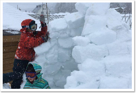 雪が降る屋外でかまくら作りをする岩崎さんの子供2人を写した写真