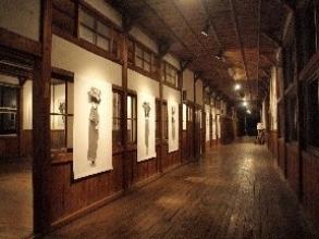 床や天井や壁が木造の廊下を、等間隔に壁に設置され天井の間接照明で照らされているアート作品が並ぶ様子を撮影した写真