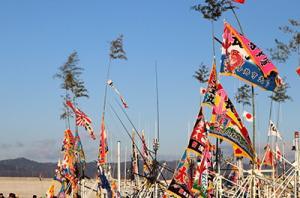 青空の下、砂浜で行われているイベントにてたくさんの旗が掲げられている写真。