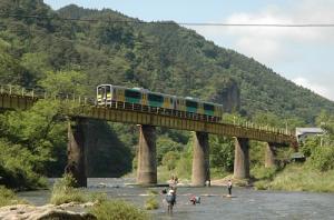 鉄橋を渡る2両の気動車と、その下の川で川遊びをする人々の写真