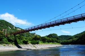 川にかかっている赤色のつり橋のあゆのつり橋を、快晴の日に下から眺めた様子の写真