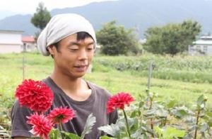 ダリアの栽培している白いタオルを頭に巻いた男性と赤い花を付けたダリアの写真