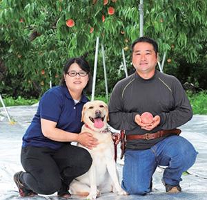 膝立ちで桃を手に載せている男性と、犬を抱いている女性の写真