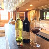 ワイナリーで、グラスハンガーにワイングラスを吊り下げ、木目の付いたカウンターに赤白2本のワインと赤ワインが注がれたワイングラスが置かれている休憩スペースの写真