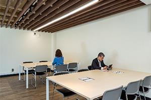 湯本駅2階に木の格子状の天井と白い壁の部屋に6人掛けの広い机が2台あり、それぞれに男性と女性が座っている写真