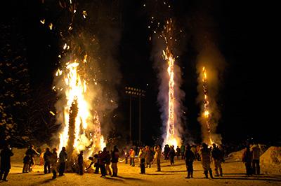 3本の巨大な火だるまの柱が夜空に燃え上がっており、それをたくさんの人々が見守っている雪と火のまつりの様子の写真
