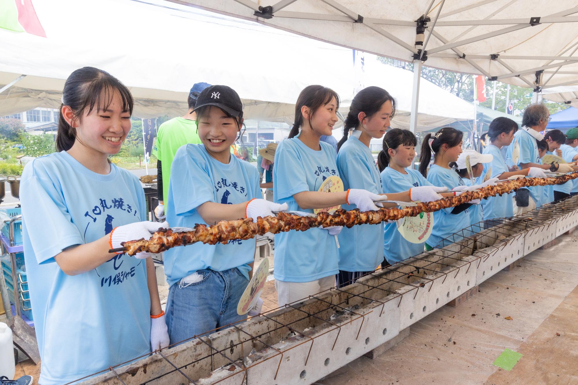 川俣町の一大イベント「かわまたシャモまつり」にて、町内の子供たちが協力して「世界一長い焼き鳥」に挑戦している写真